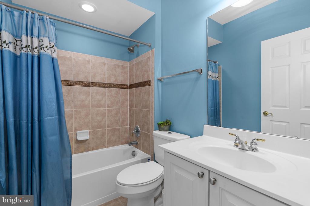 Bathroom with a tiled bathtub, blue shower curtain, toilet, and white vanity.