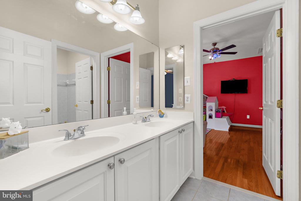 Bathroom with a long white double-sink vanity and a view into an adjoining red-walled room.