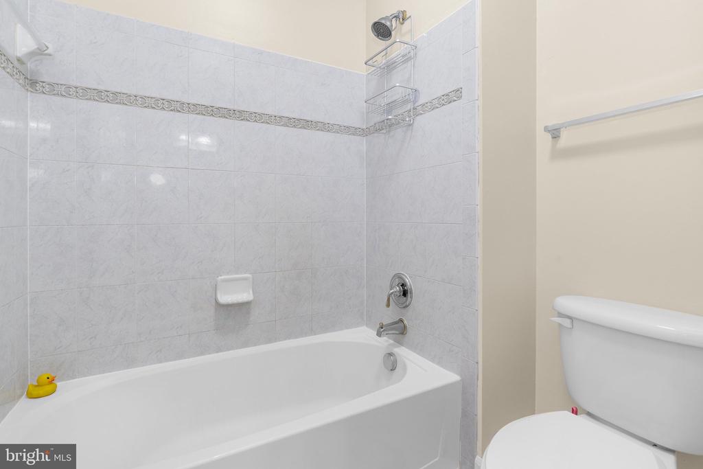 Bathroom with a white bathtub, gray tiled surround, chrome fixtures, and a yellow rubber duck.