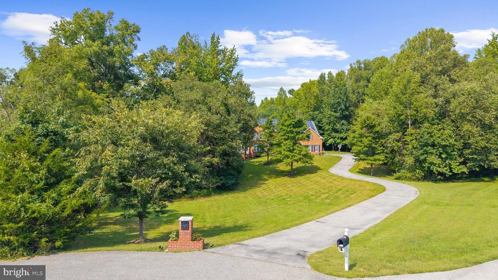 Aerial view of a brick house among trees, reached by a long curved driveway.