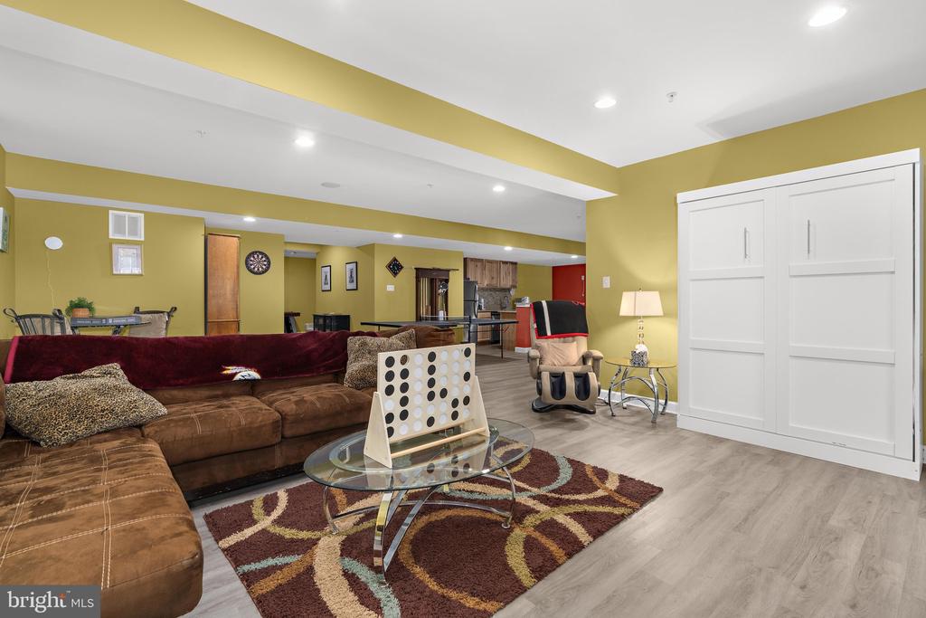 Furnished recreation room with mustard-yellow walls, brown sectional, patterned rug, and white sliding closet doors.