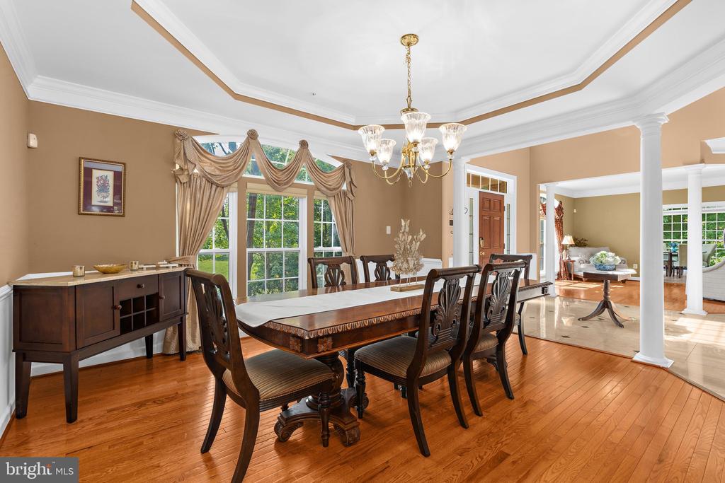 Dining room with a carved wood table, gold chandelier, hardwood floors, and a decorative tray ceiling.