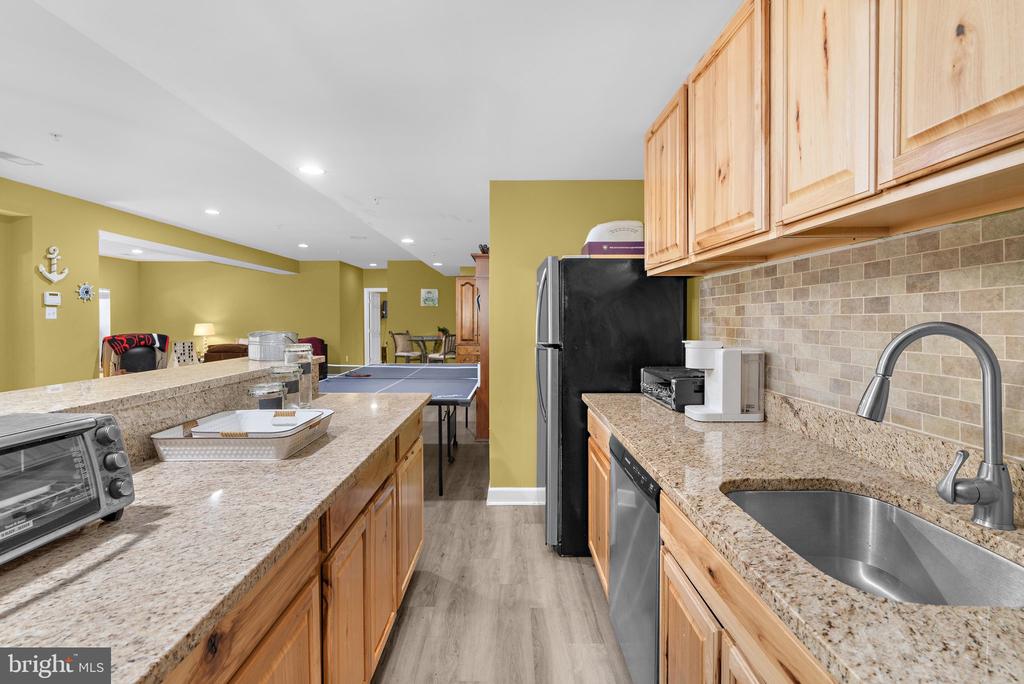 Kitchen with granite countertops, wood cabinets, stainless dishwasher, and a view into a recreation area.
