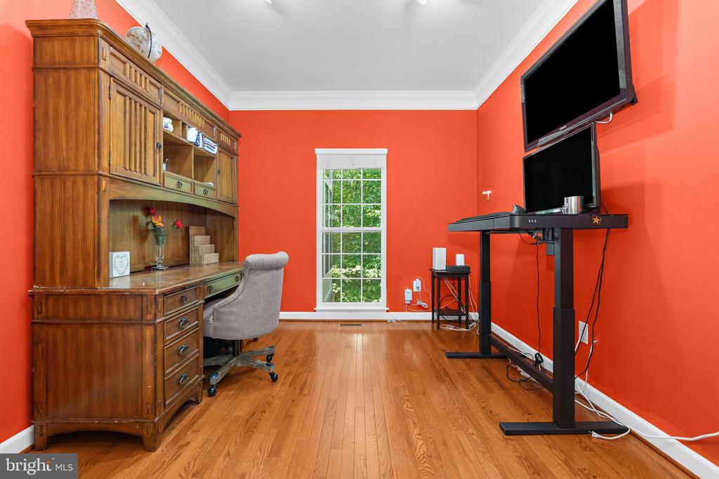 Home office with coral-red walls, hardwood floors, and wooden desk and hutch.
