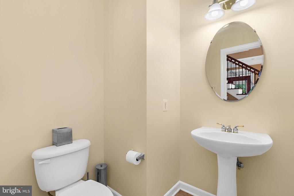 Powder room with a white pedestal sink, oval mirror, and toilet.