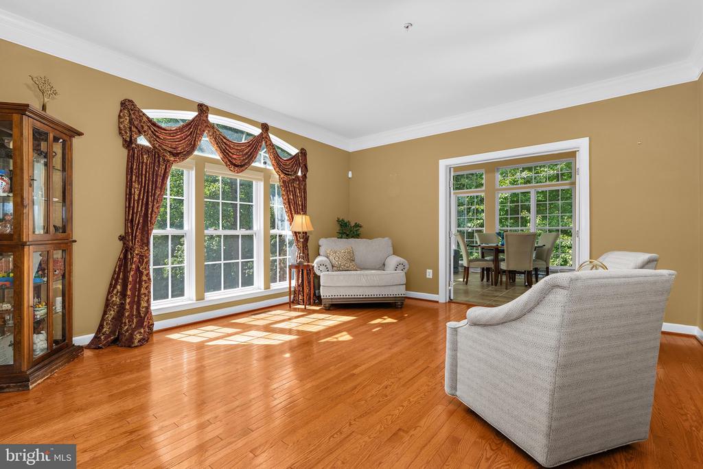 Living room with hardwood floors, large draped windows, and white armchairs.