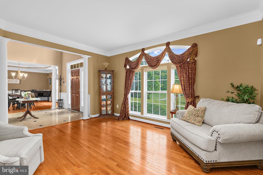 Living room with hardwood floors, neutral sofas, and a large curtained window overlooking the lawn.