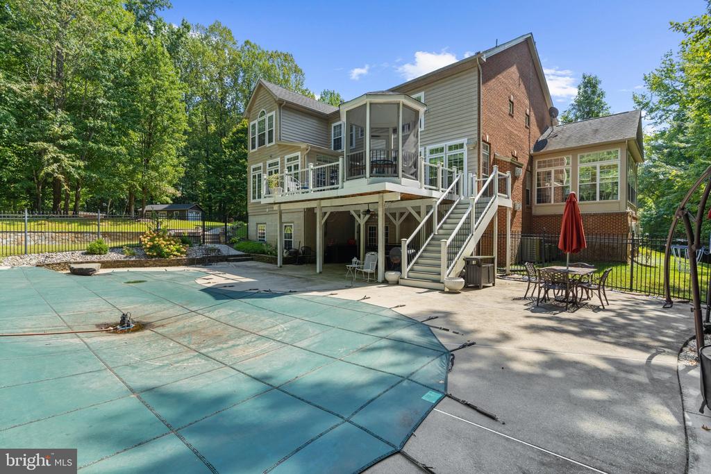 Rear of a two-story home with a raised deck and screened porch beside a covered pool.
