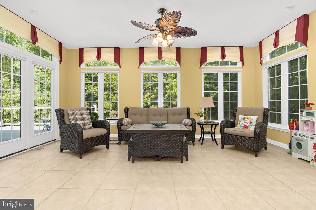 Furnished sunroom with dark wicker seating, yellow walls, and large windows overlooking trees.
