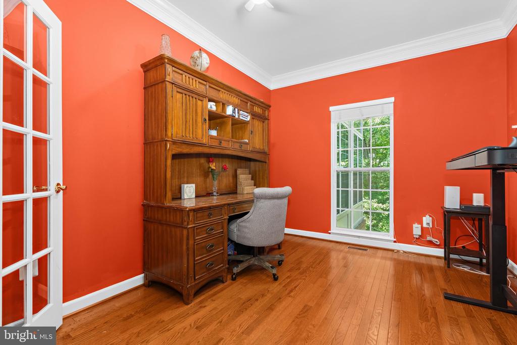 Home office with orange walls, hardwood floors, a wooden desk and hutch, and tall windows.