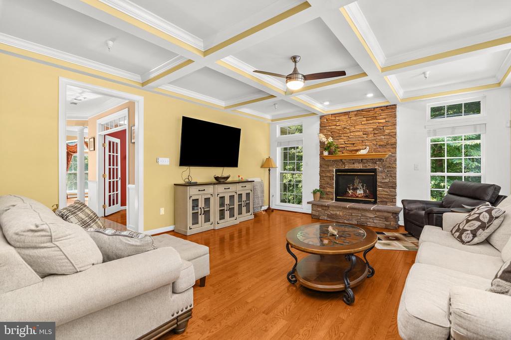 Furnished living room with a stone fireplace, coffered ceiling, and warm hardwood floors.