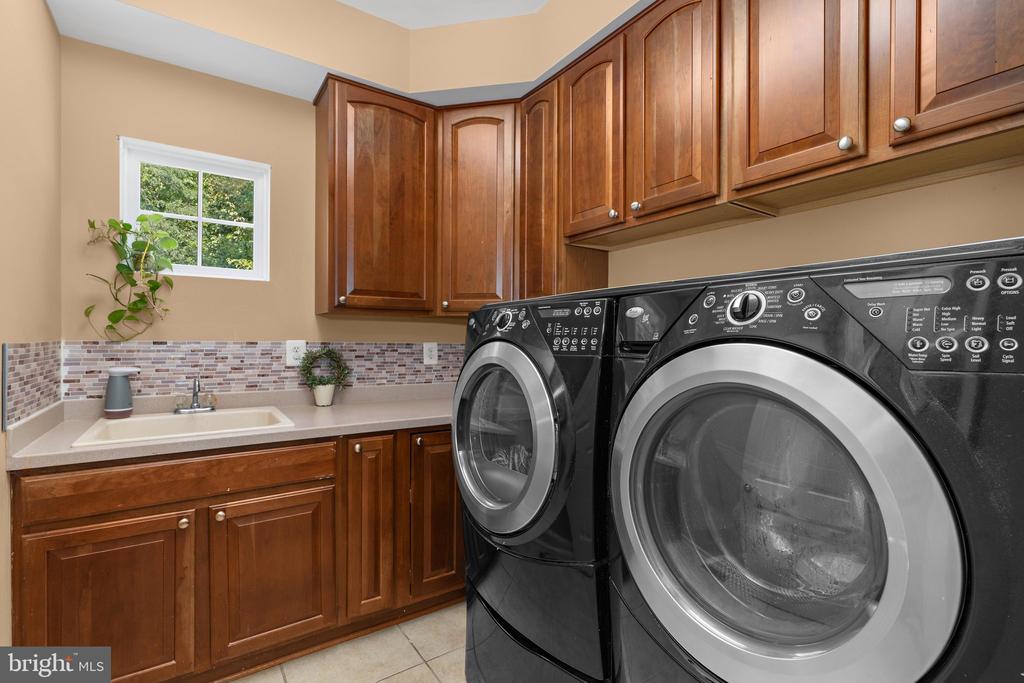 Laundry room with front-loading washer and dryer, wood cabinetry, utility sink, and window.
