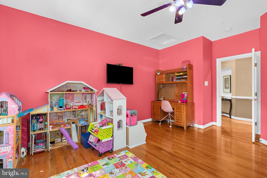Children’s playroom with pink walls, toy houses, a wooden desk, and hardwood floors.