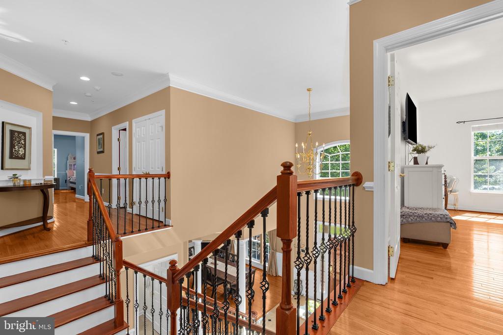 Upstairs landing with a polished wood staircase and wrought-iron railing beside an open bedroom doorway.