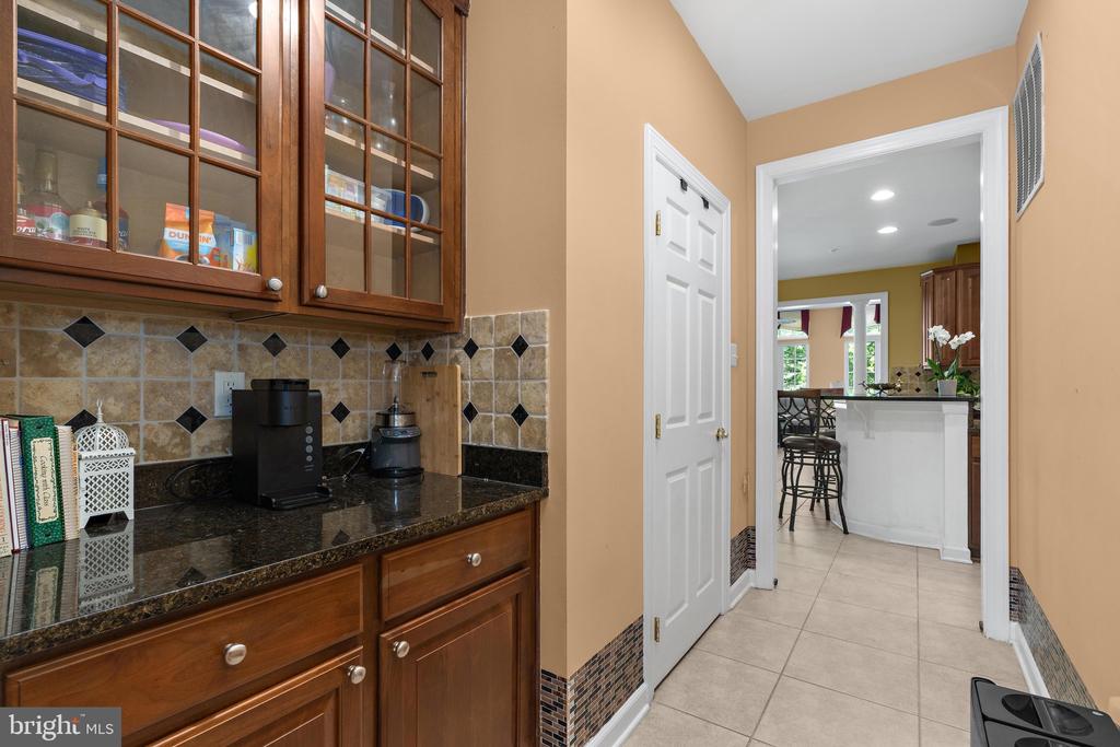 Kitchen with dark wood cabinetry, granite counters, and a tile backsplash beside an opening to the island.