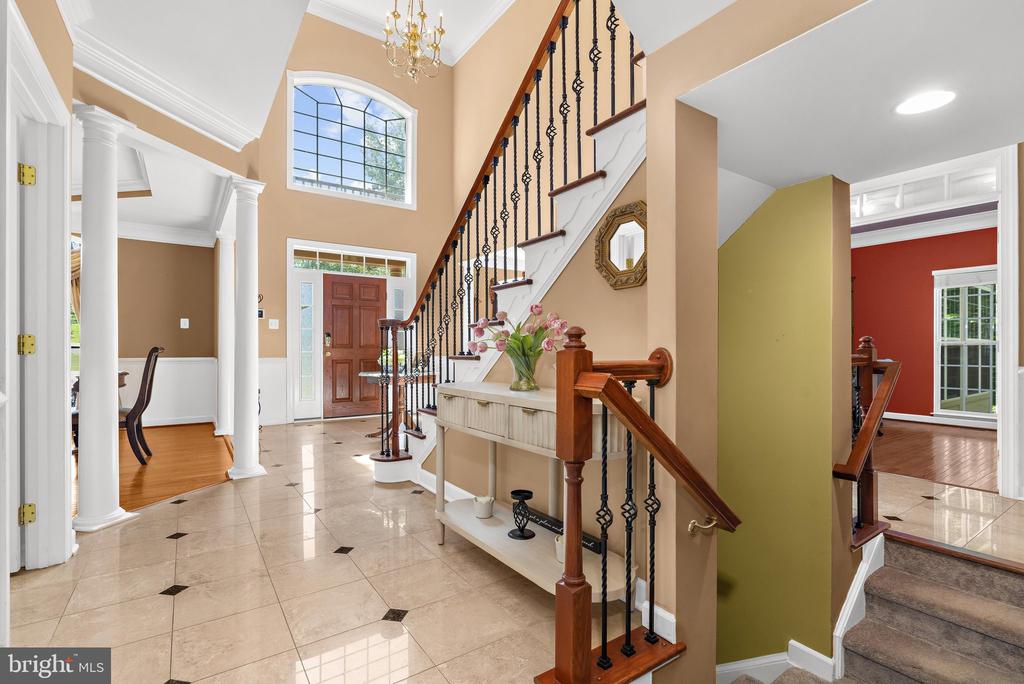 Foyer with tiled floors, white columns, an arched window, and a wood staircase with iron railings.