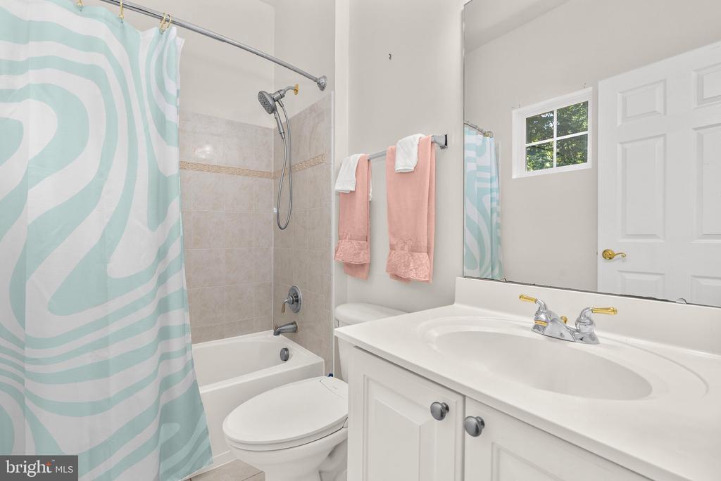 Bathroom with a white vanity, tub and shower behind a mint-and-white patterned curtain, and coral towels.