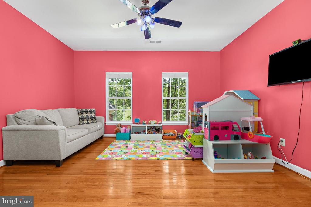 Playroom with coral-pink walls, a gray sofa, hardwood floors, and children's toys.