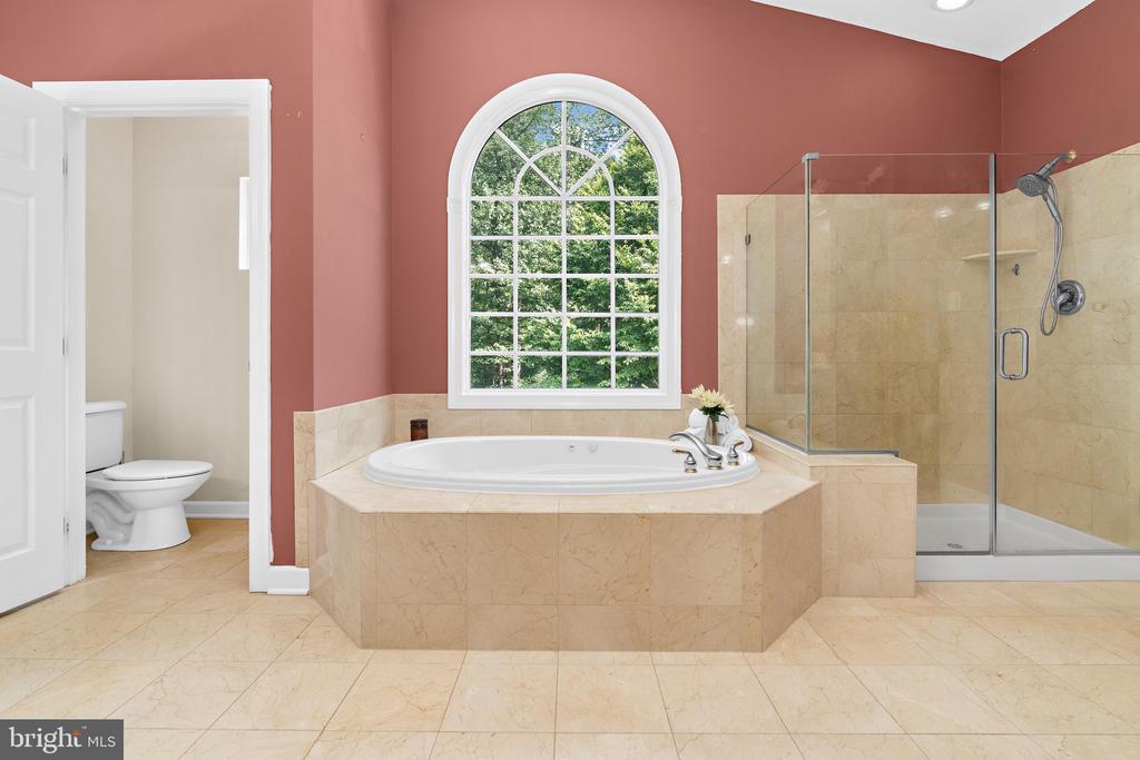 Bathroom with a built-in soaking tub beneath an arched window and glass-enclosed shower.