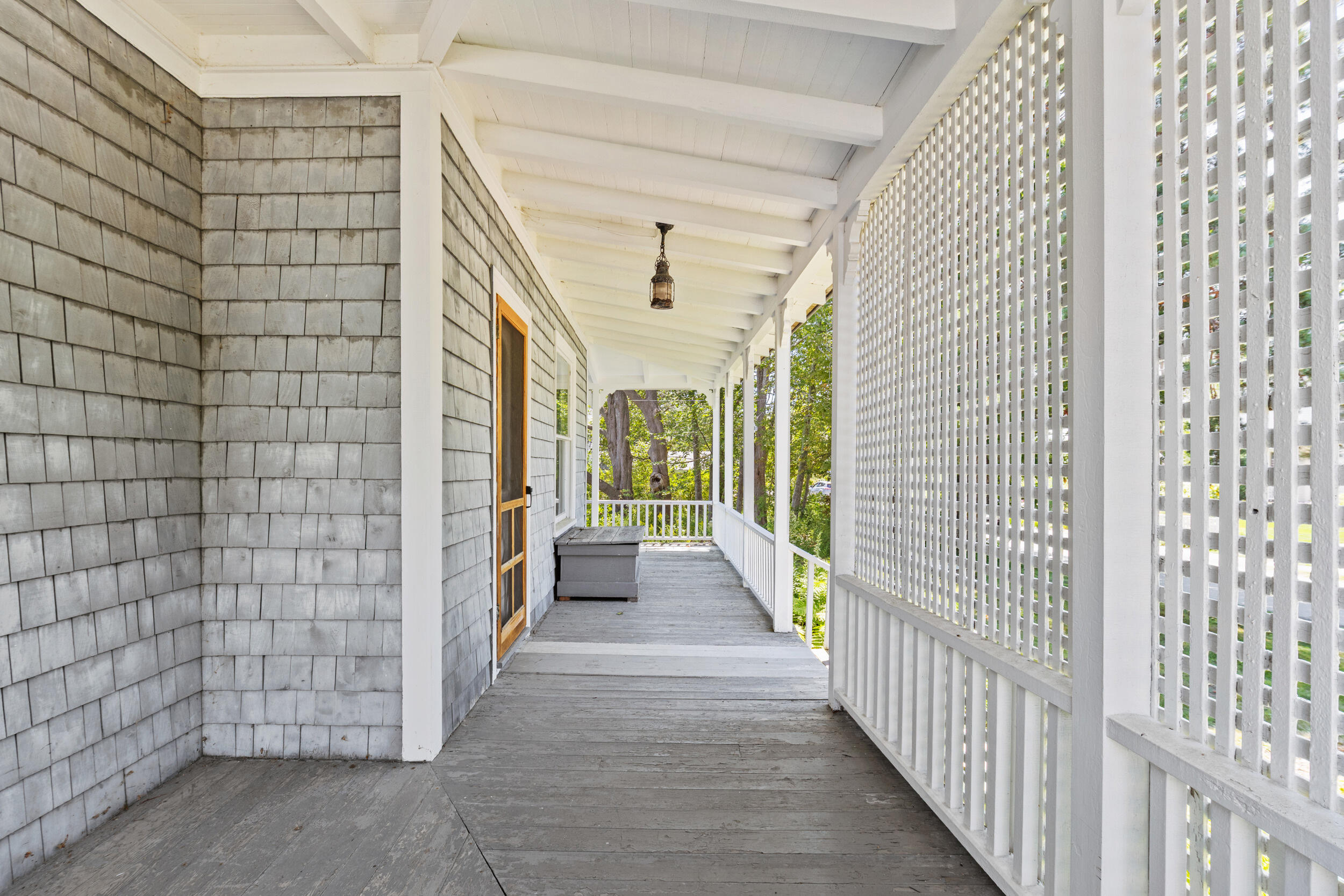 Covered porch with gray shingle siding, white lattice panels, and a weathered wooden deck.