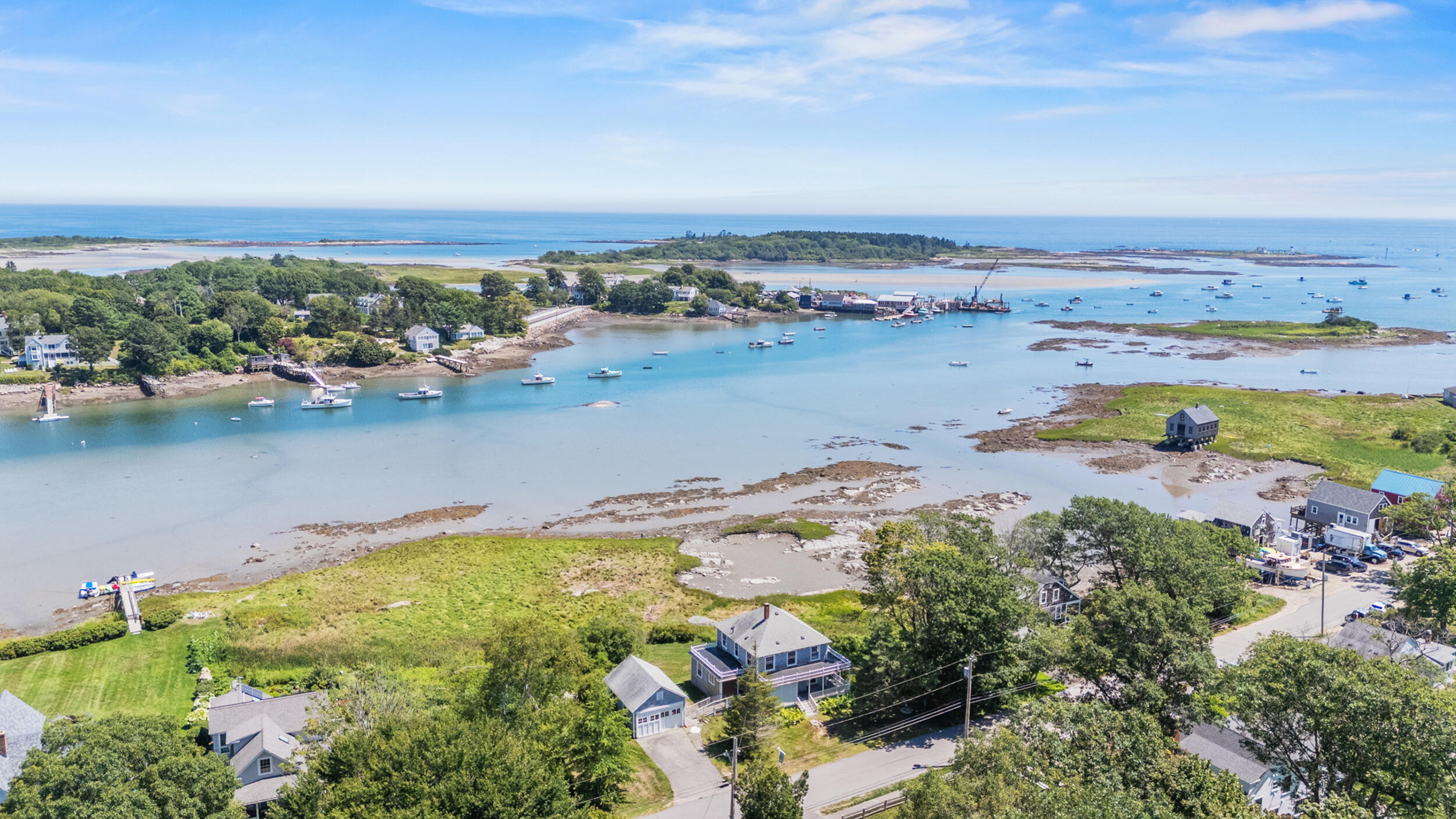 Aerial view of a coastal harbor with shoreline homes, boats, and exposed tidal flats.
