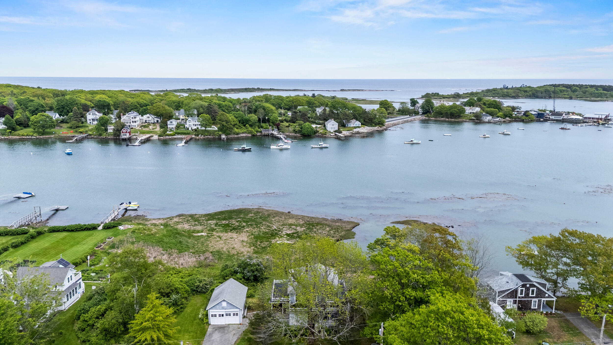 Aerial coastal view of waterfront homes and boats across a broad inlet.