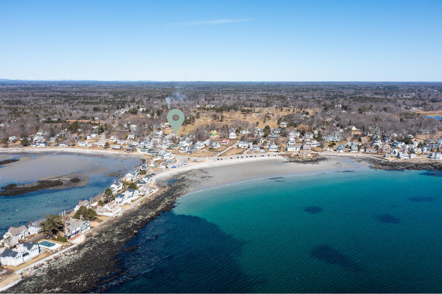 Aerial view of a coastal neighborhood, with houses along rocky shores and beaches beside blue water.