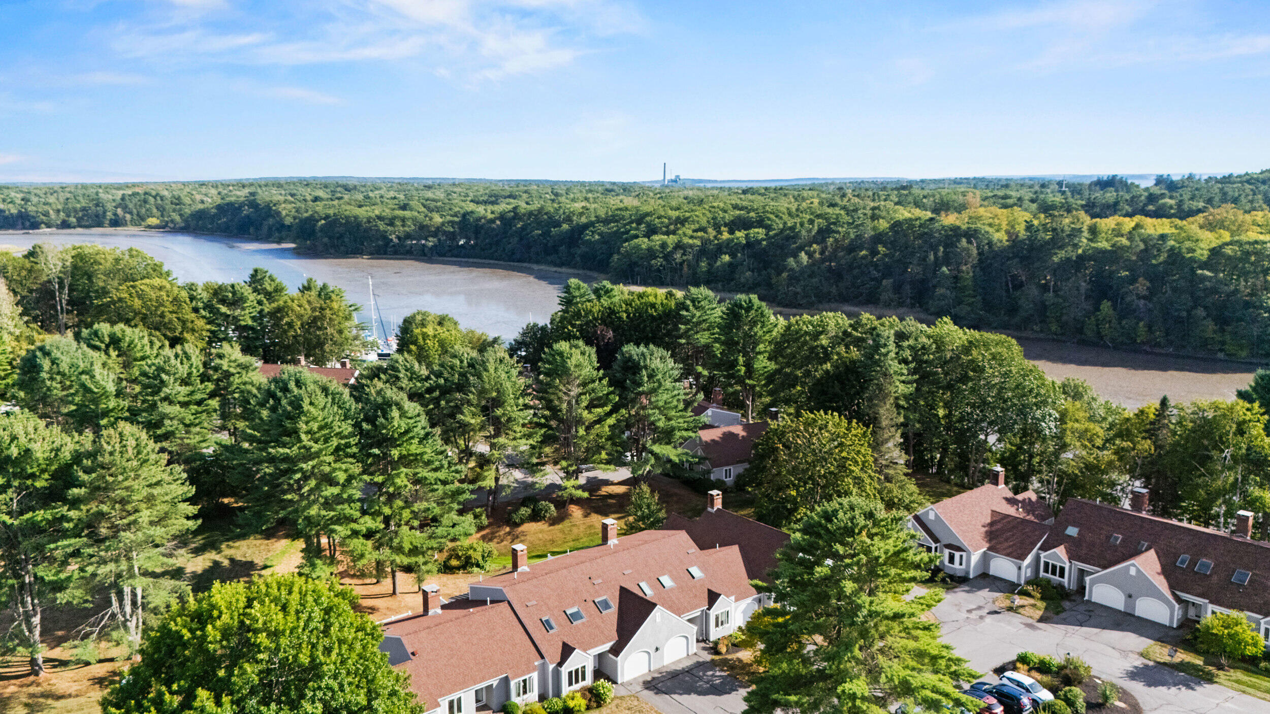 Aerial view of homes and wooded shoreline beside a winding tidal cove at low tide.