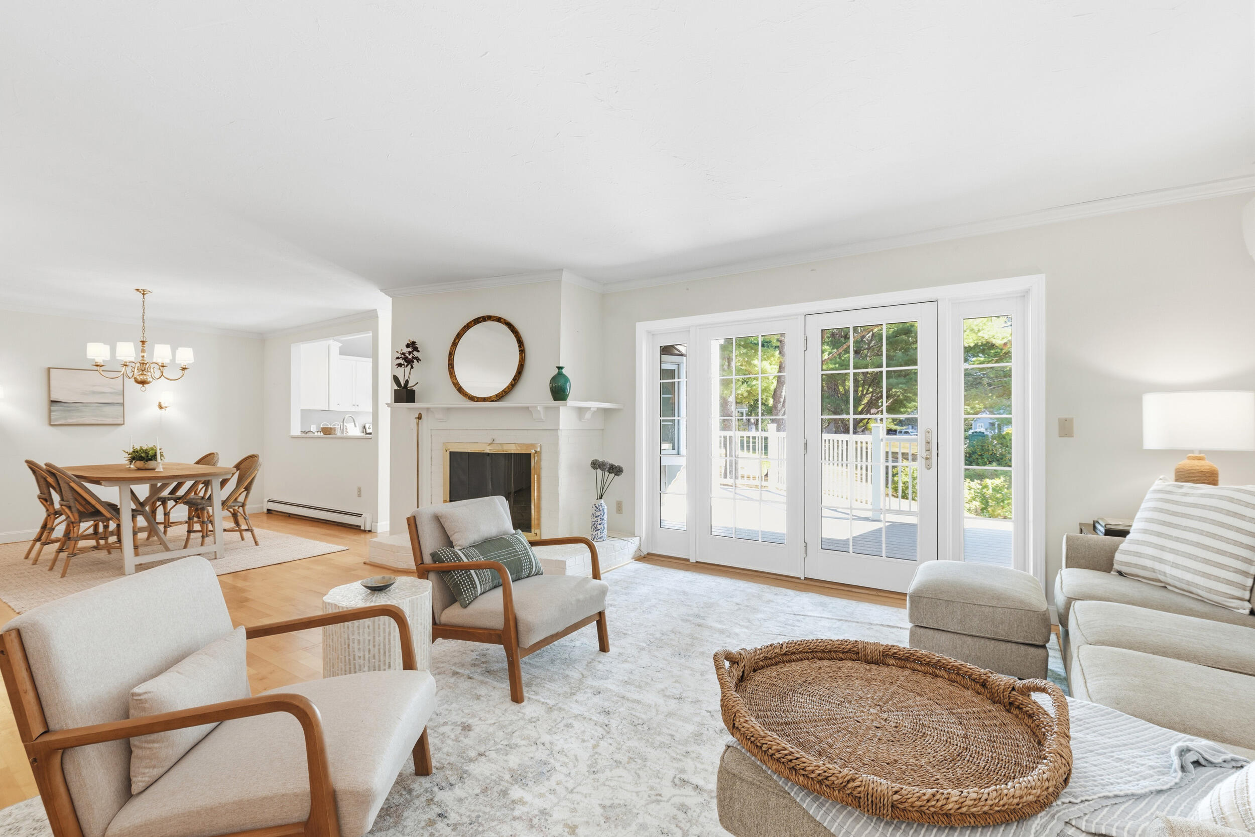 Staged living room with a white fireplace, dining area, and French doors opening to a deck.