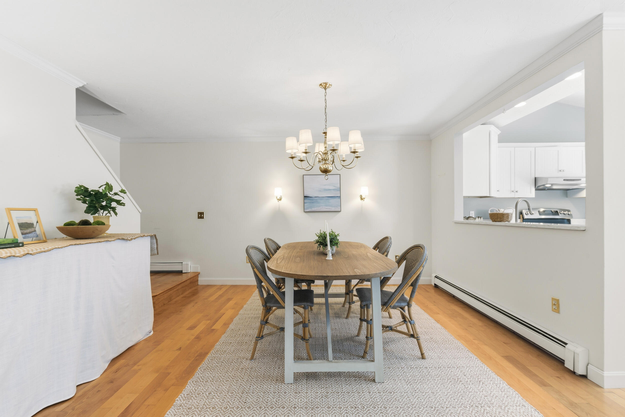 Dining room with a wood table, woven chairs, brass chandelier, and pass-through to the kitchen.