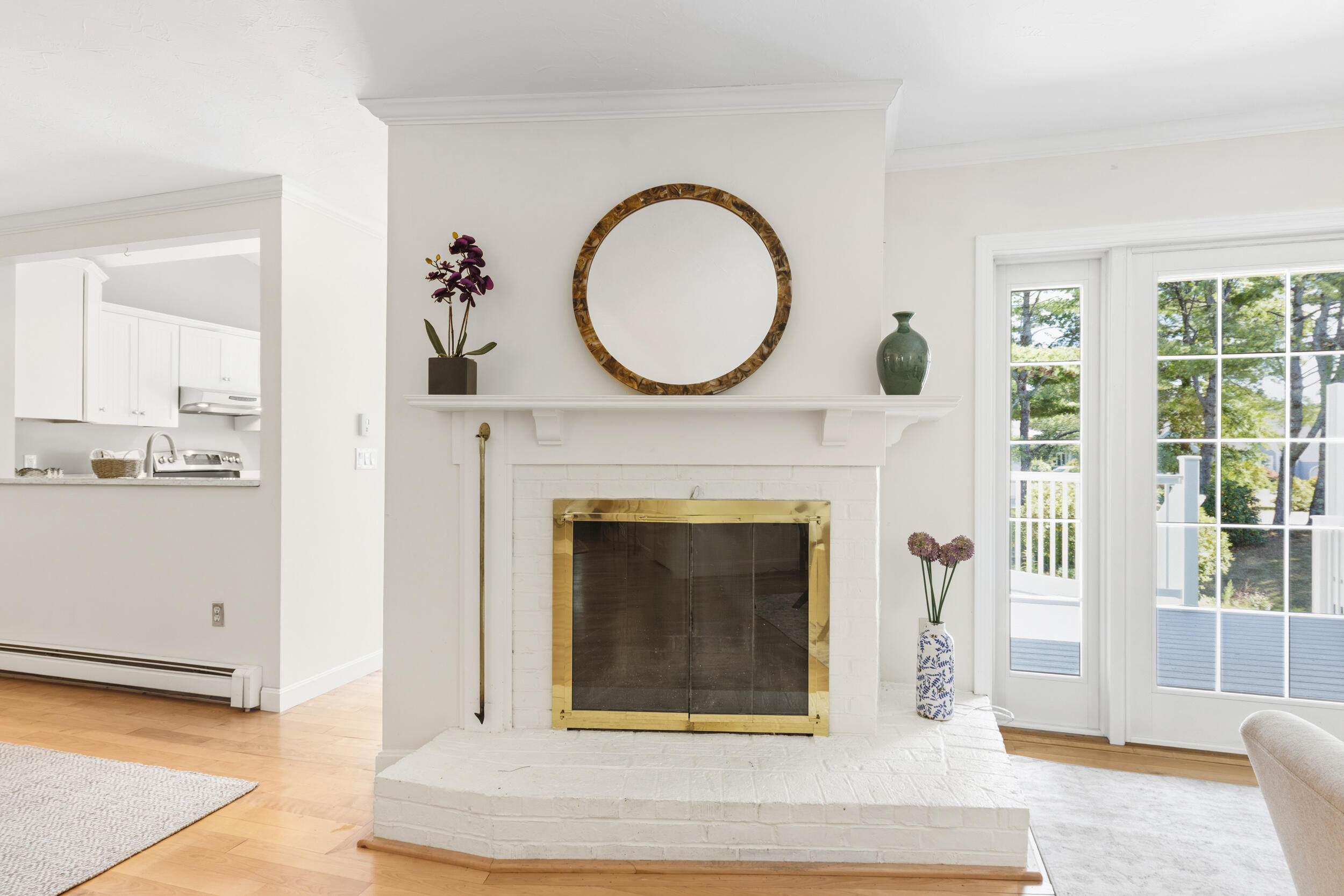 Living room with a white brick fireplace, brass fire screen, and glass doors opening onto a deck.