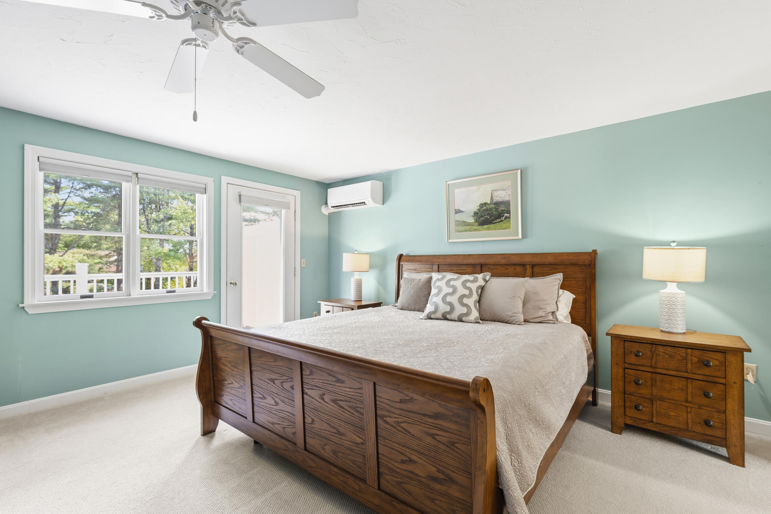 Furnished bedroom with a large wooden bed, aqua walls, and windows overlooking leafy trees.