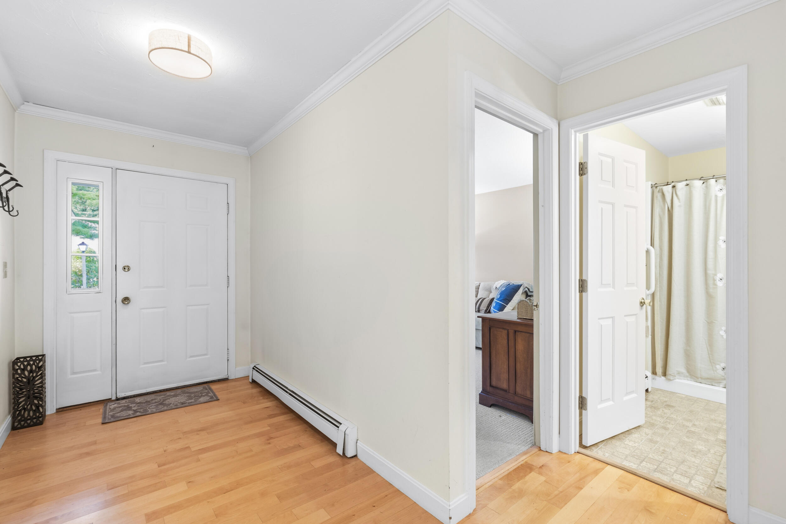 Entry foyer with hardwood floors, a front door with sidelight, and open doorways to a bathroom and living room.