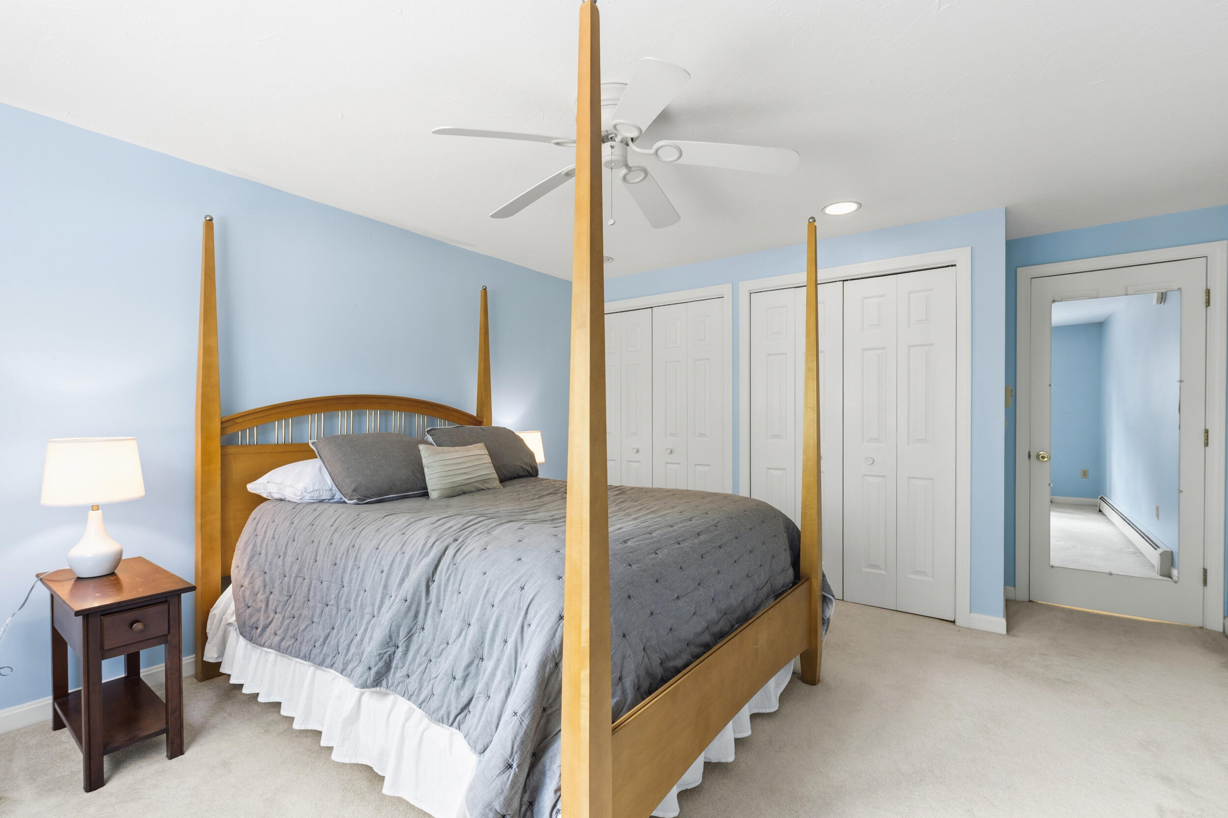 Bedroom with a wooden four-poster bed, gray bedding, pale blue walls, and white closet doors.