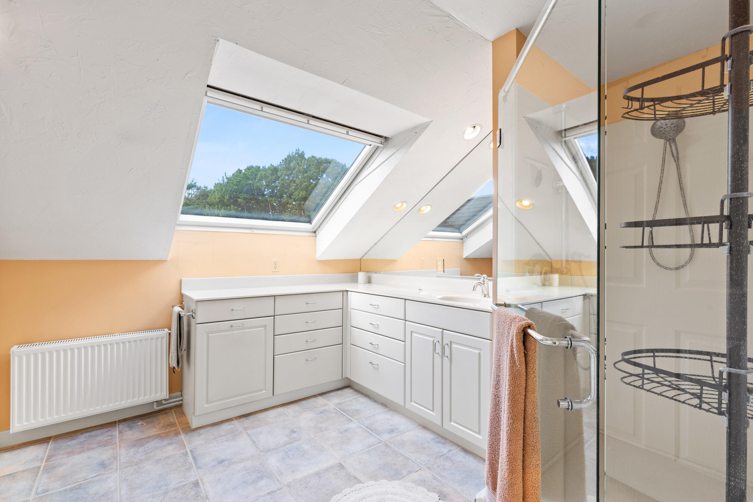 Attic bathroom with white vanity, glass shower, and large skylights.