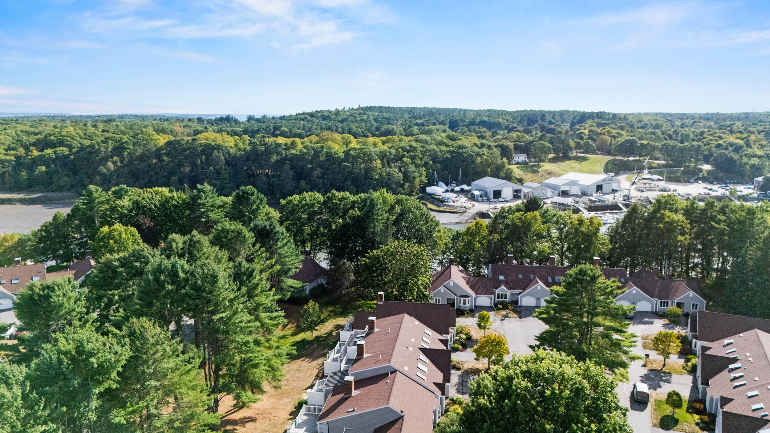 Aerial view of townhouse homes among trees, with a boatyard and sailboats beyond.