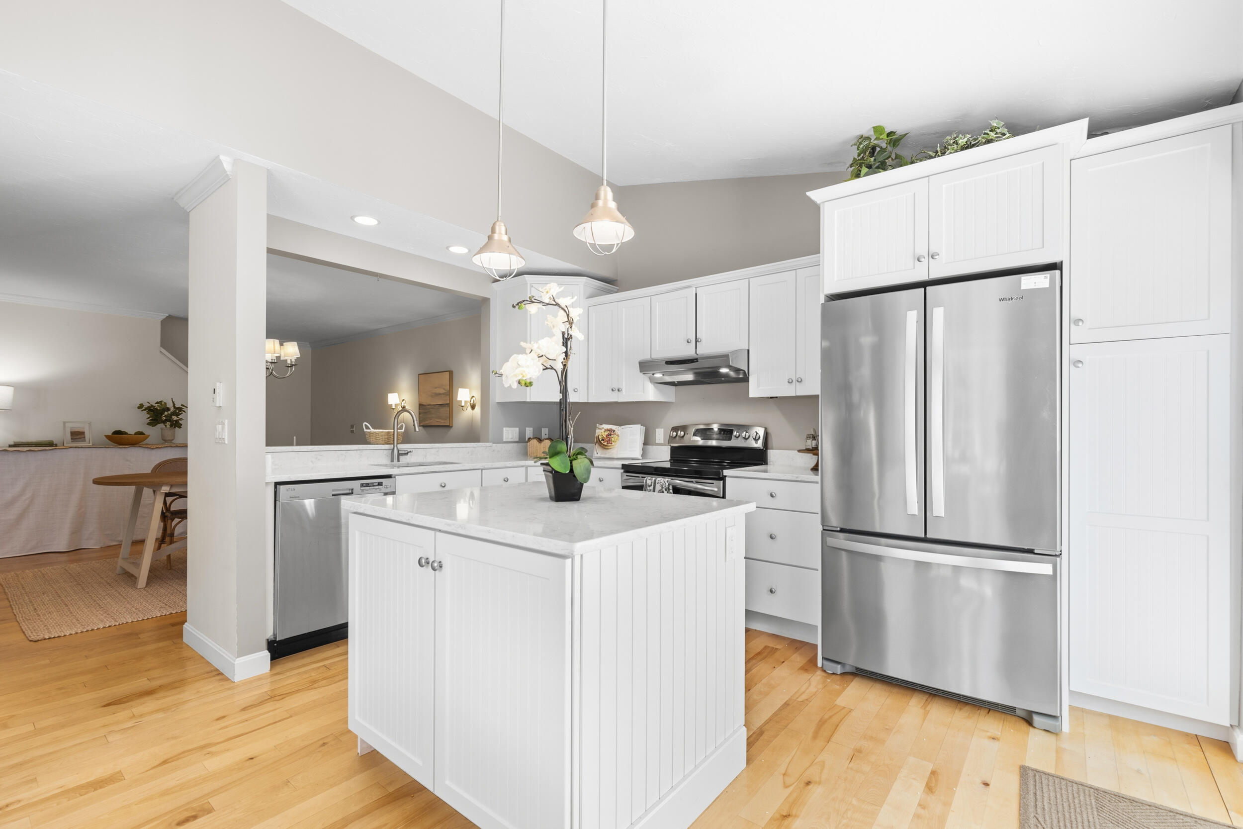 Bright white kitchen with a central island, stainless steel appliances, and light wood floors.