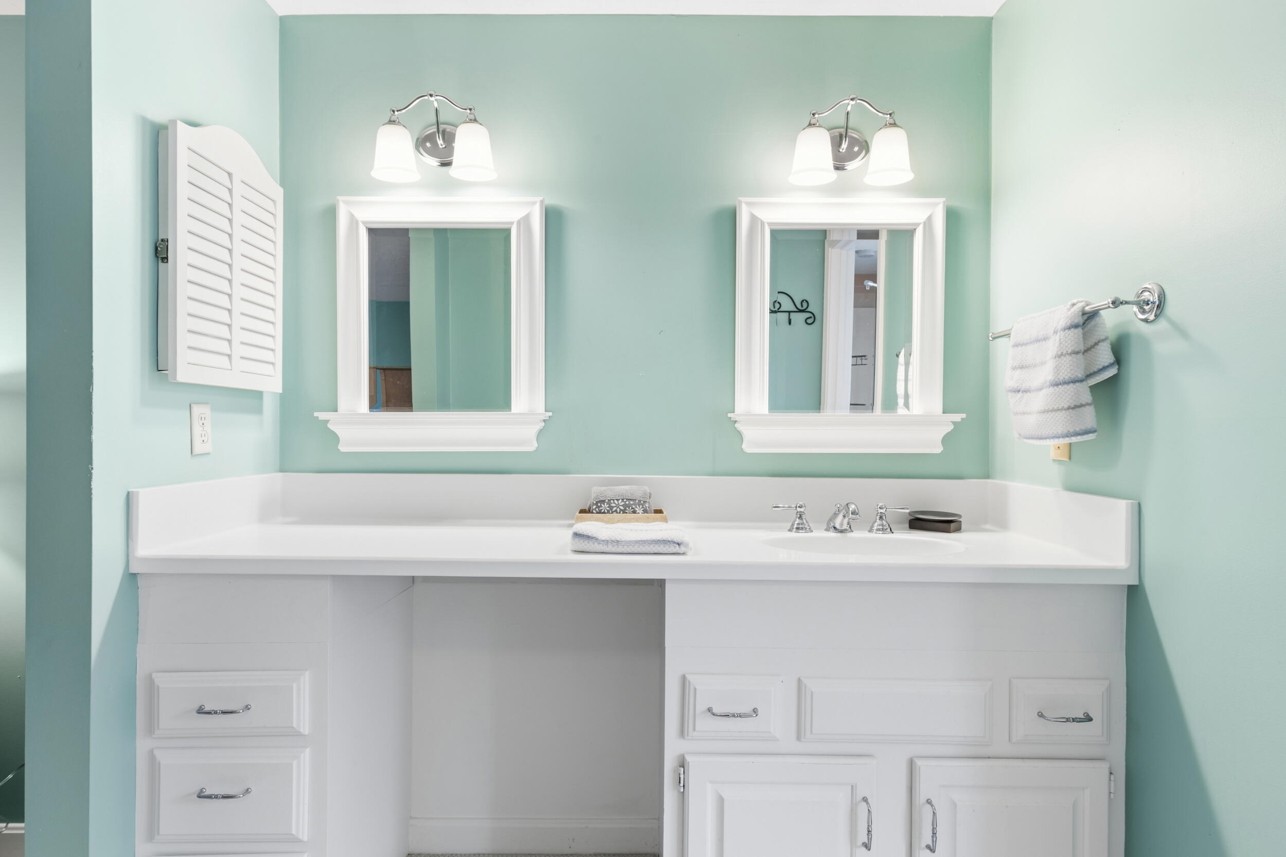 Bathroom vanity with two framed mirrors, white cabinetry, chrome fixtures, and pale aqua walls.