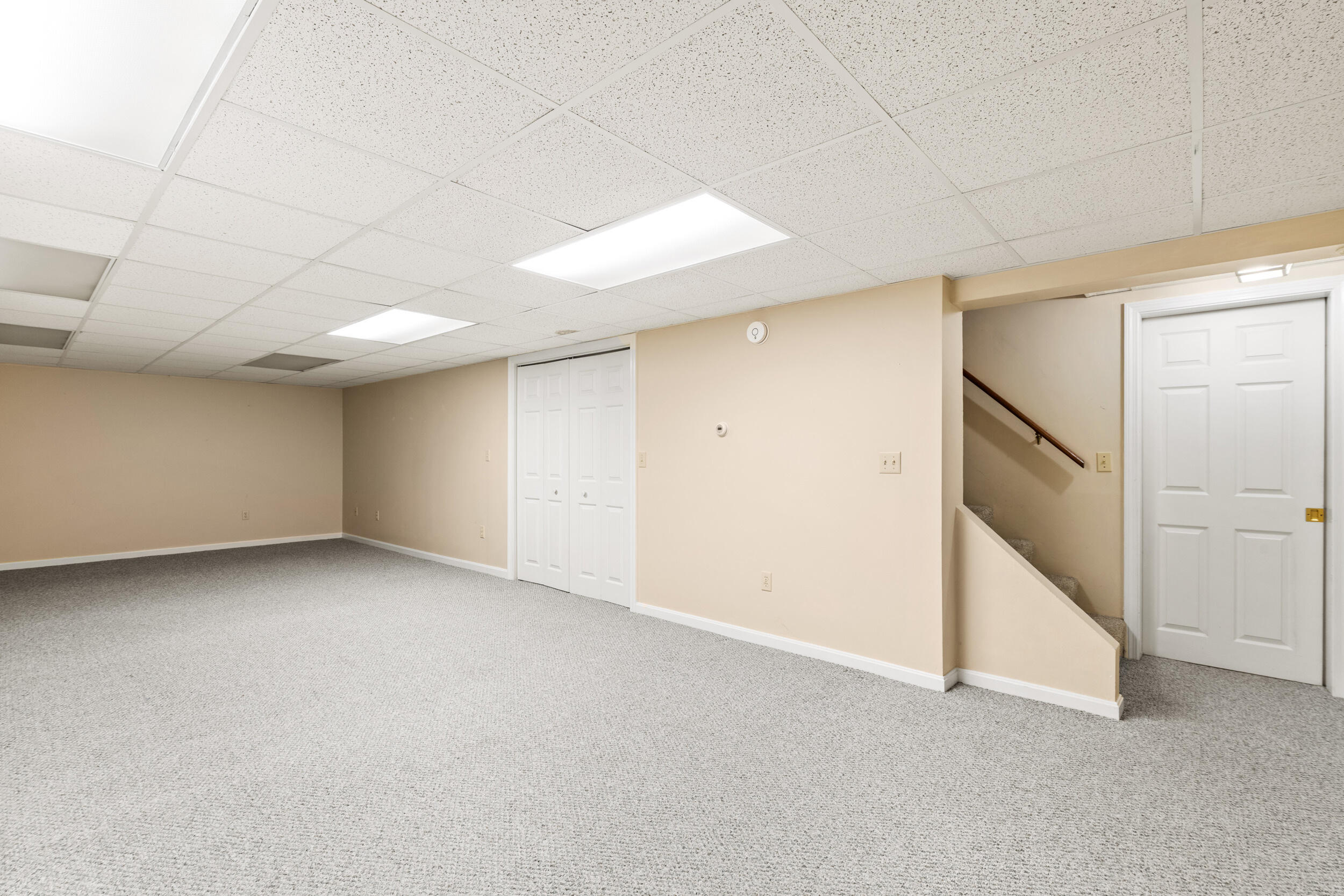 Finished basement with gray carpeting, double closet doors, and stairs beside a white door.