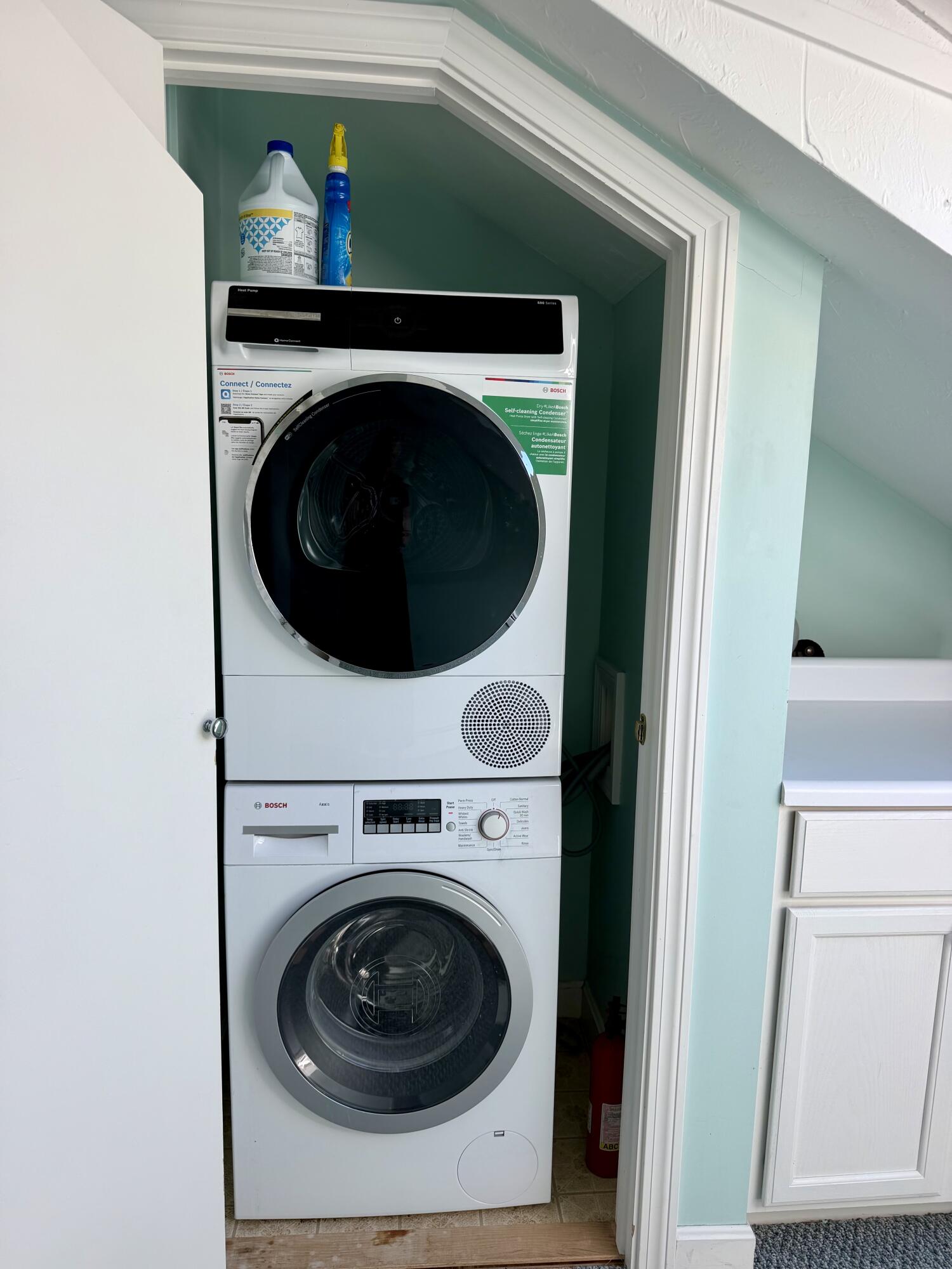 Stacked Bosch washer and dryer tucked into a compact laundry closet beneath a sloped ceiling.