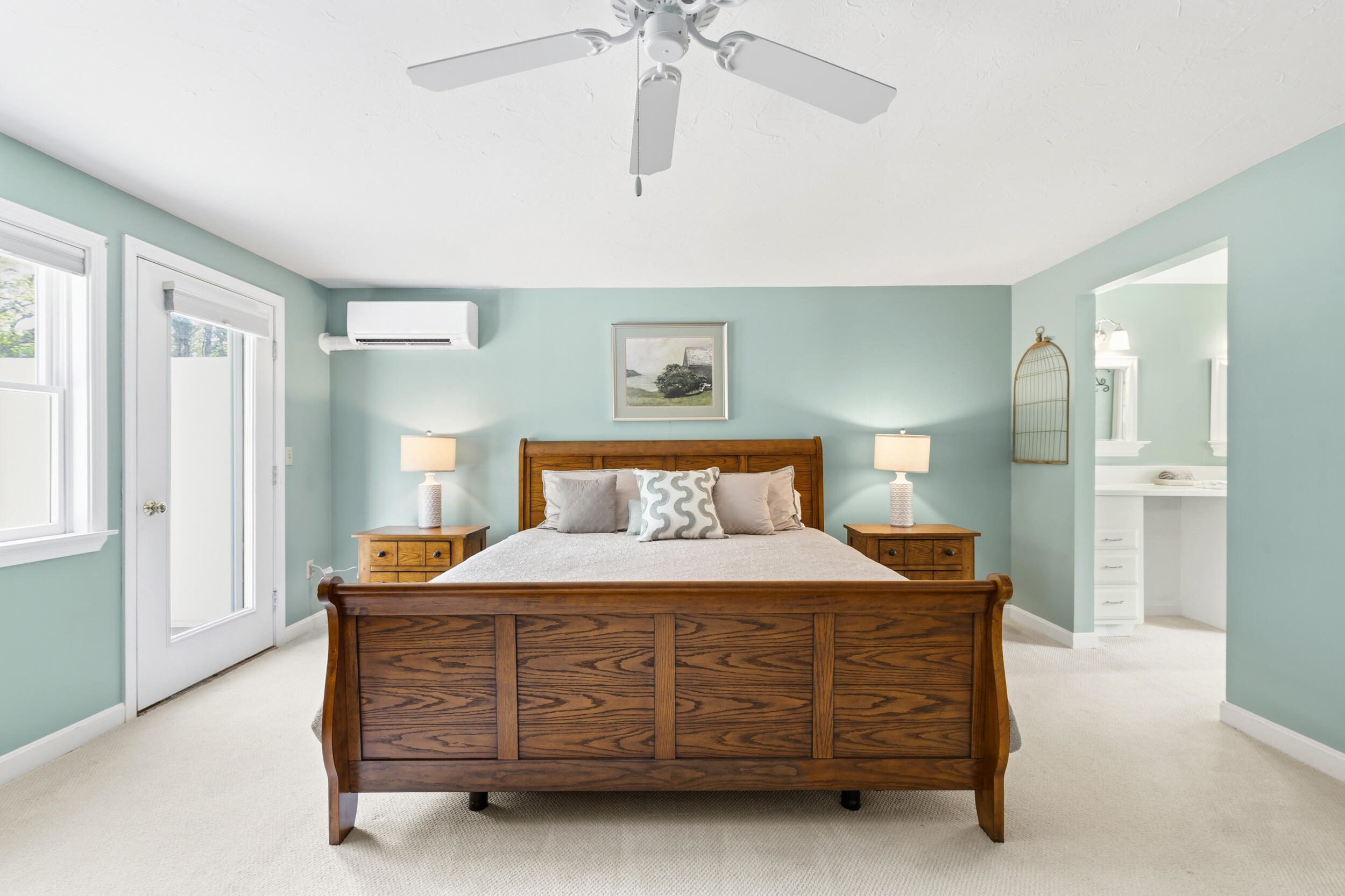 Bedroom with a wooden bed, pale blue-green walls, and an open doorway to the bathroom.
