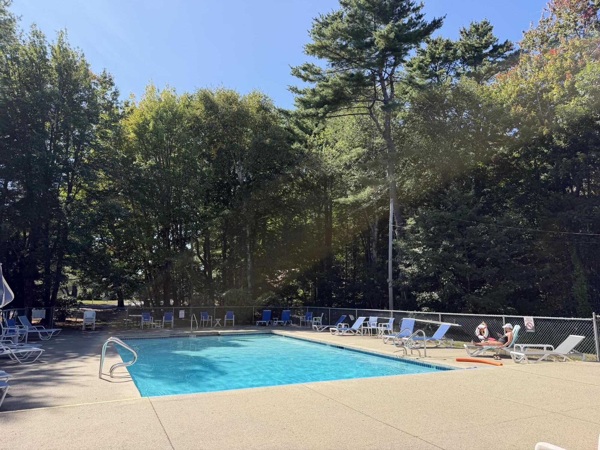 Outdoor swimming pool with turquoise water, lounge chairs, and a wooded backdrop.