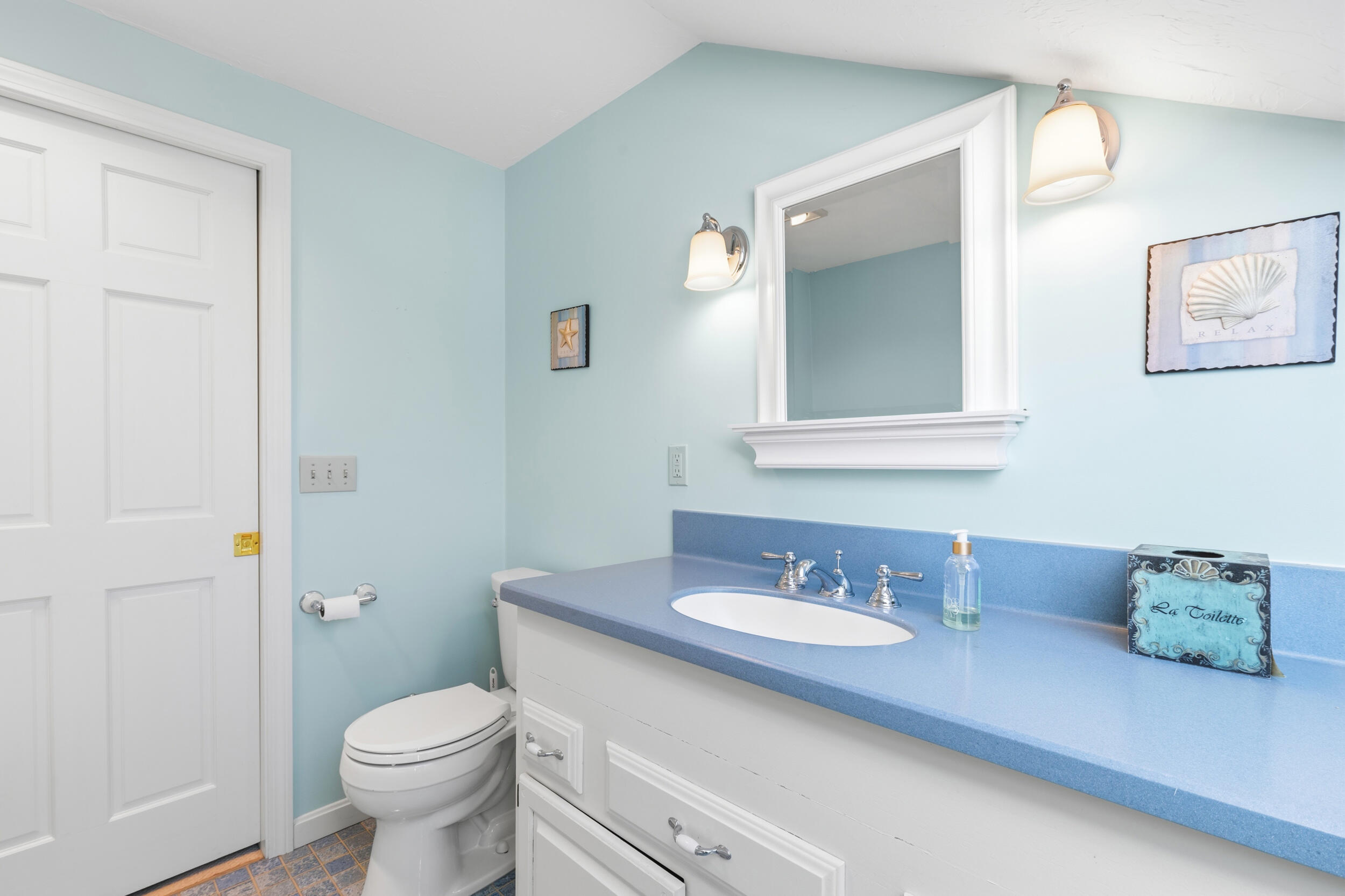 Bathroom with pale blue walls, blue countertop, white vanity, and coastal-themed decor.