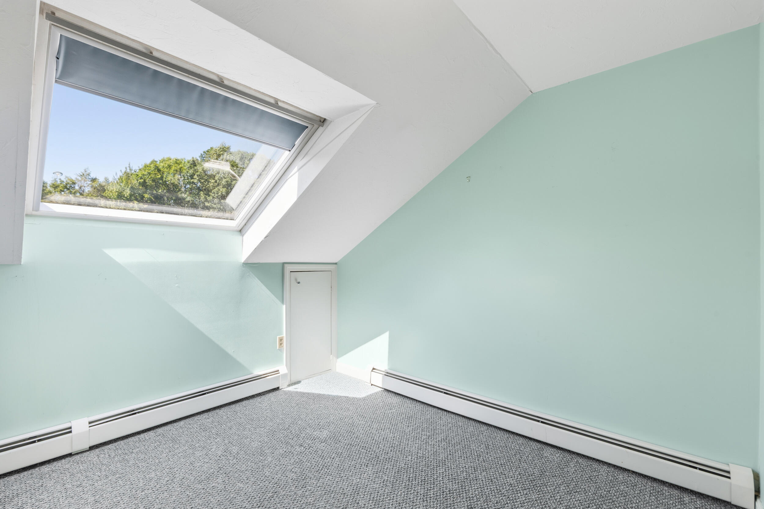 Empty carpeted room with pale mint walls, a sloped ceiling, and a large skylight.