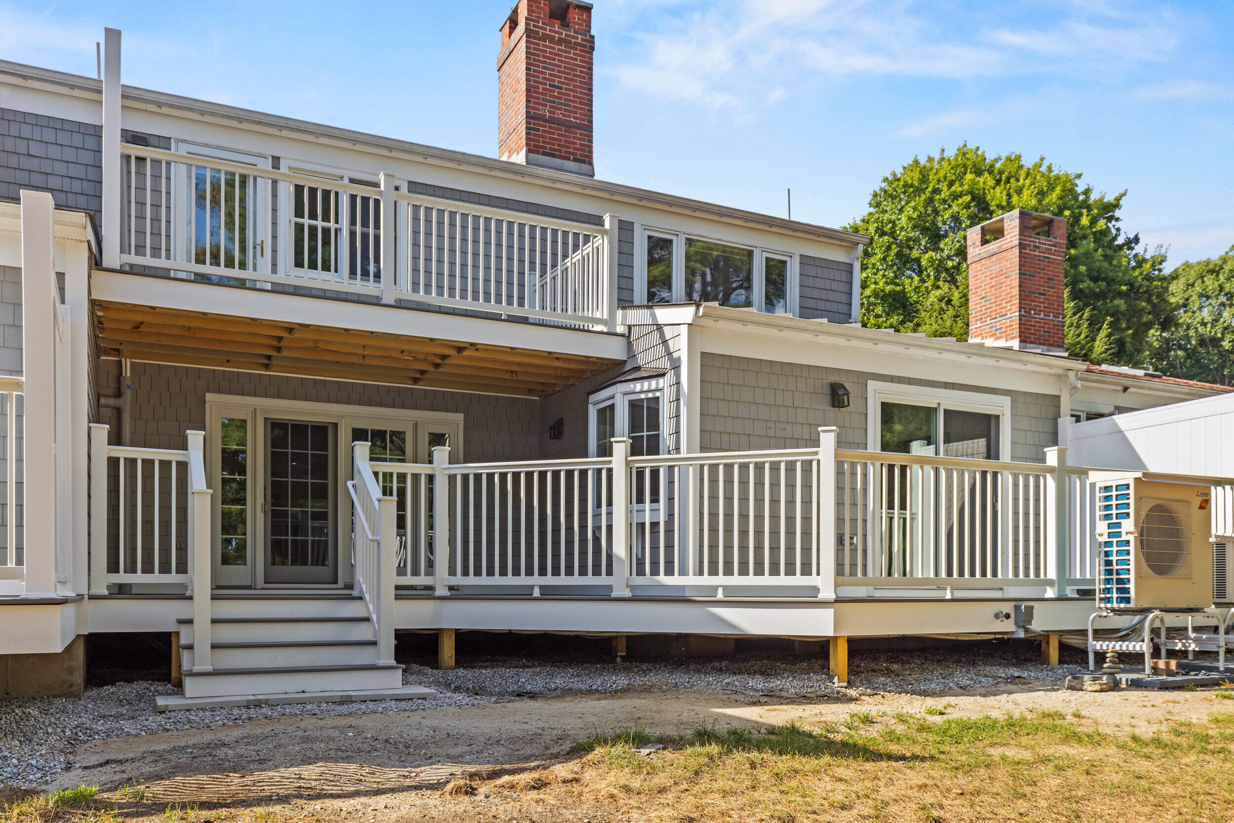 Gray shingle-sided home with white-railed decks, stairs, and two brick chimneys.