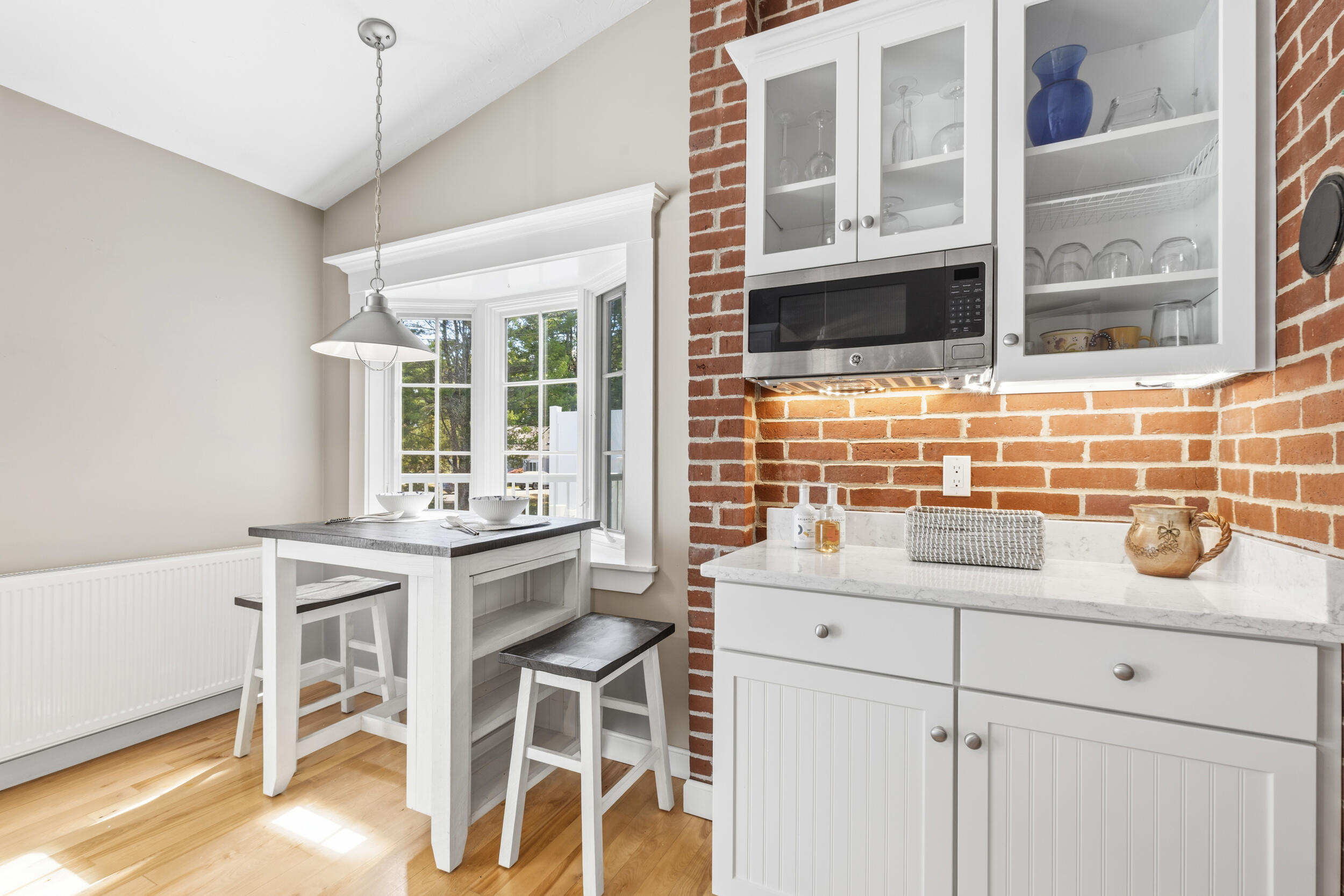 Bright kitchen with a red brick backsplash, white cabinets, and a breakfast table beside a bay window.