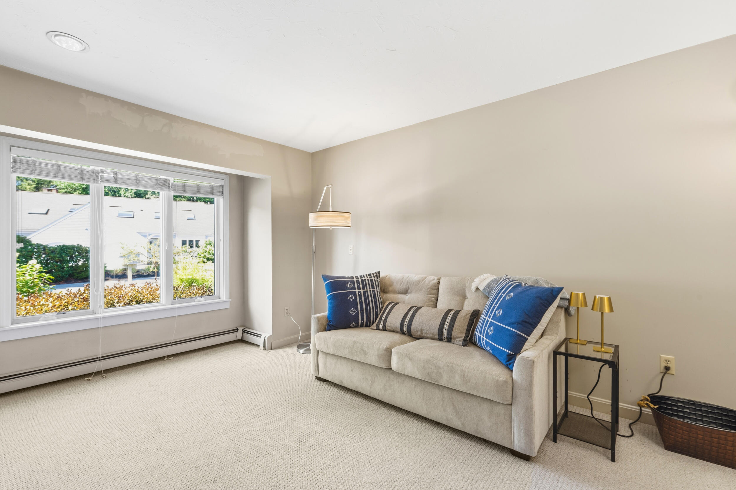 Furnished living room with a light sofa, blue patterned cushions, and a large window with blinds.