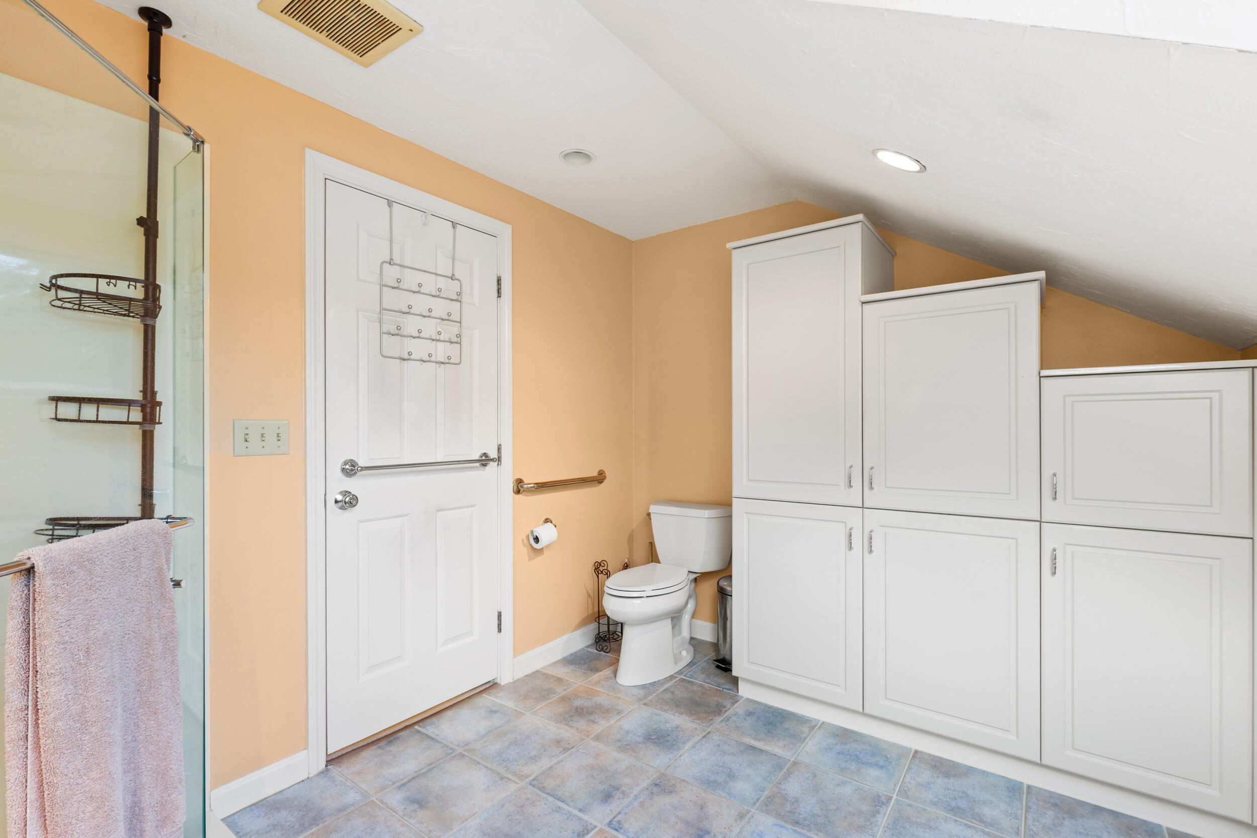 Bathroom with glass shower, white built-in cabinets, and blue-gray tile flooring.