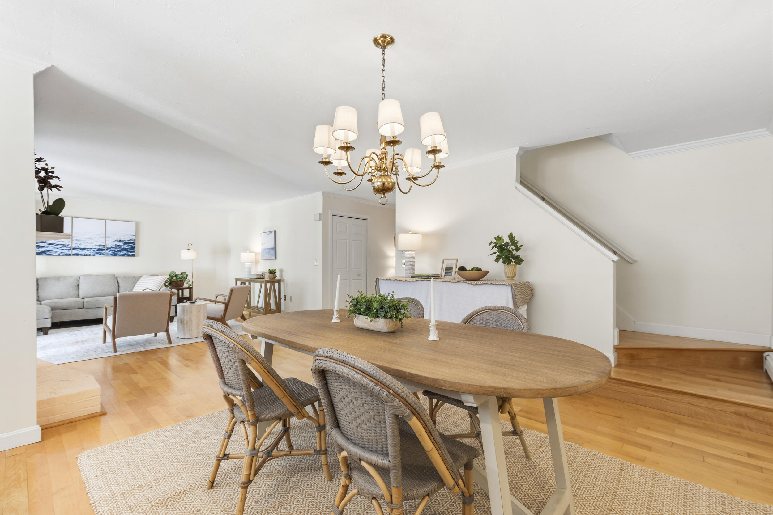 Dining room with an oval wood table, woven chairs, brass chandelier, and adjoining living room.