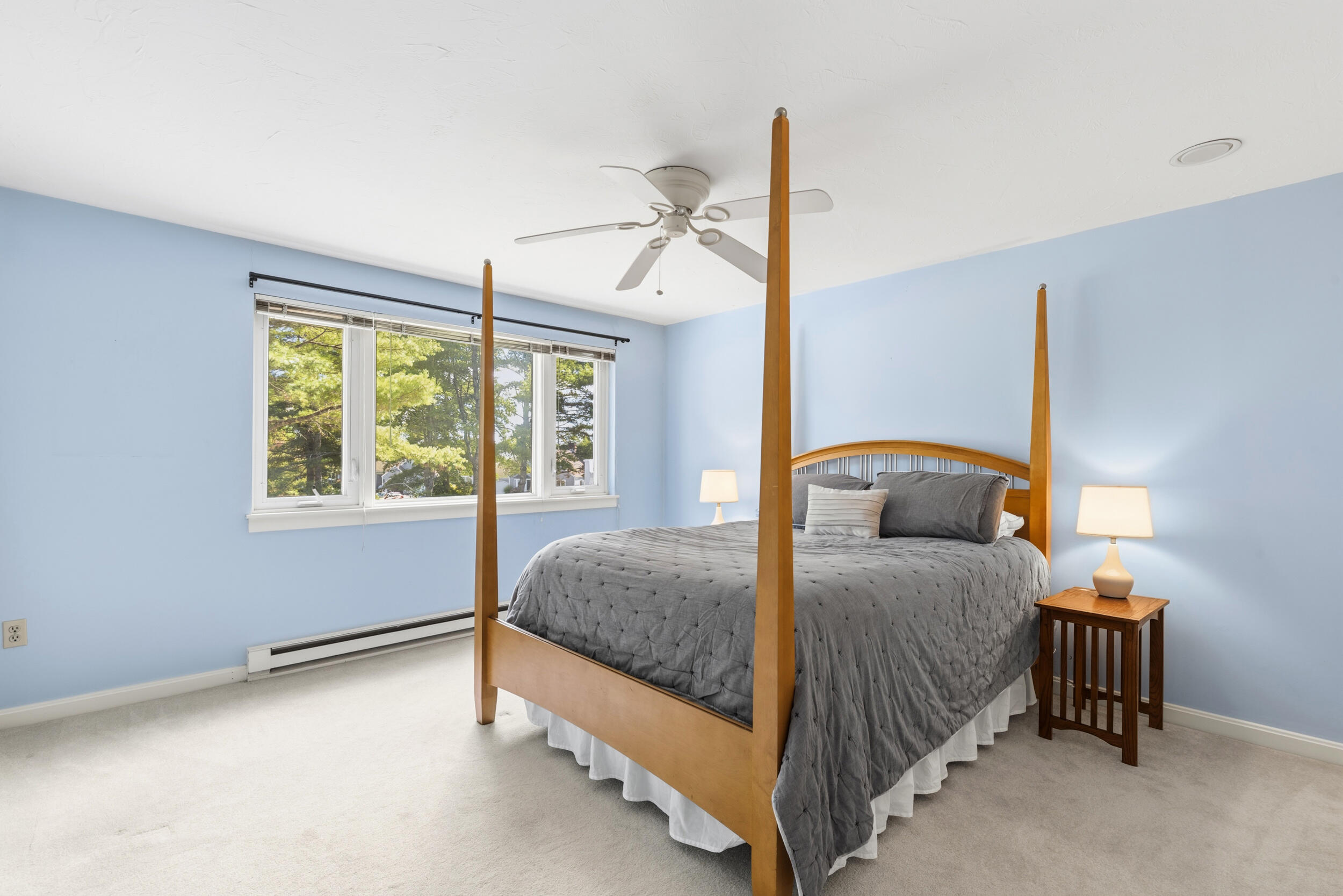 Bedroom with a gray four-poster bed and a wide window overlooking leafy trees.